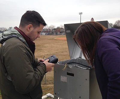A UNCC student and MCAQ Monitoring staff member install a personal particulate matter sensor at Garinger Air Quality Monitoring Station for a collocation study.